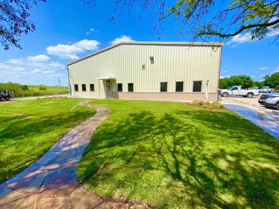 A light-colored metal commercial building sits on a green lawn with a curved stone pathway leading to the entrance.