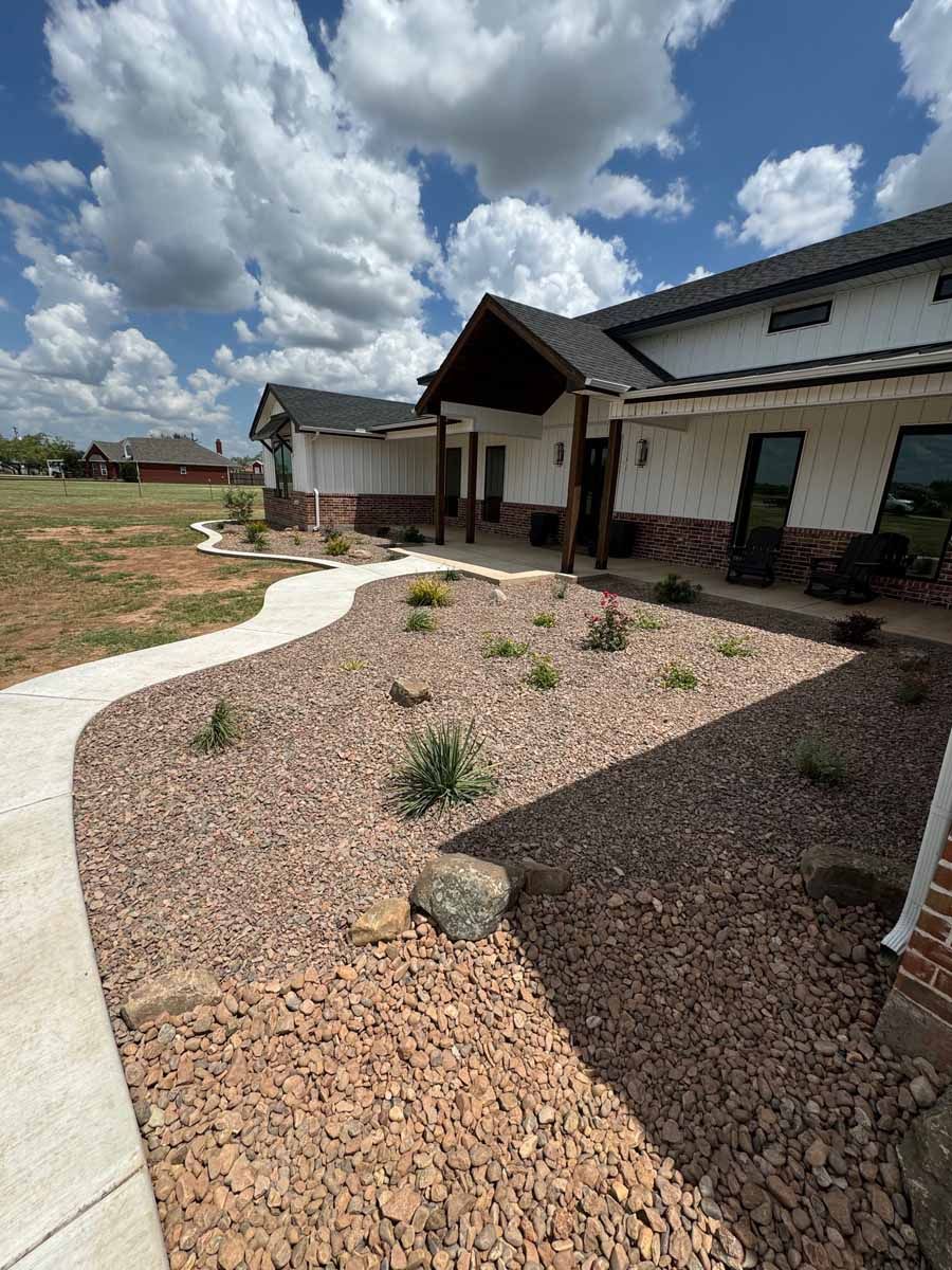 A modern white farmhouse with stone accents and a covered porch, fronted by a gravel landscape and concrete walkway.