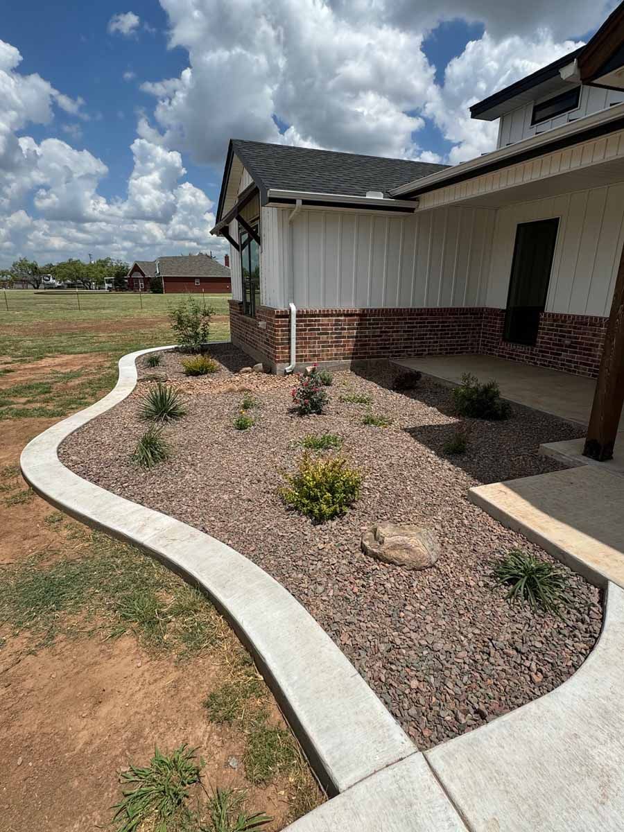 A modern house with white vertical siding and brick, featuring a curved concrete landscape border and rock flower bed.