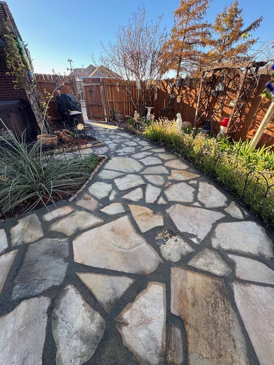 A flagstone garden path leads toward a wooden gate in a backyard setting under a clear blue sky.