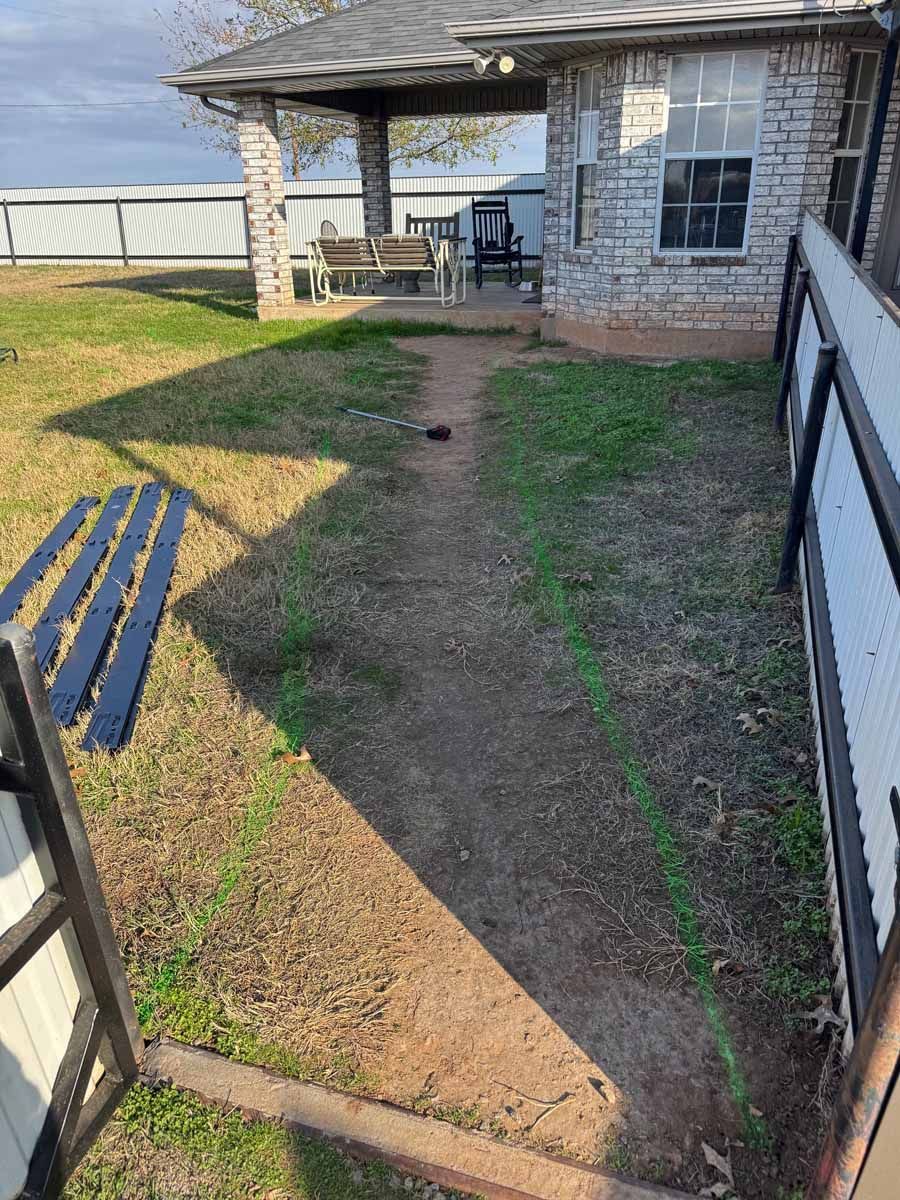A dirt path outlined in green spray paint leads across a lawn toward the covered patio of a brick house.