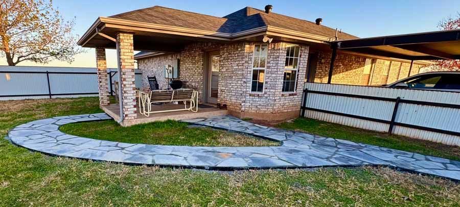A brick house features a curved stone walkway leading to a covered front porch with outdoor furniture.