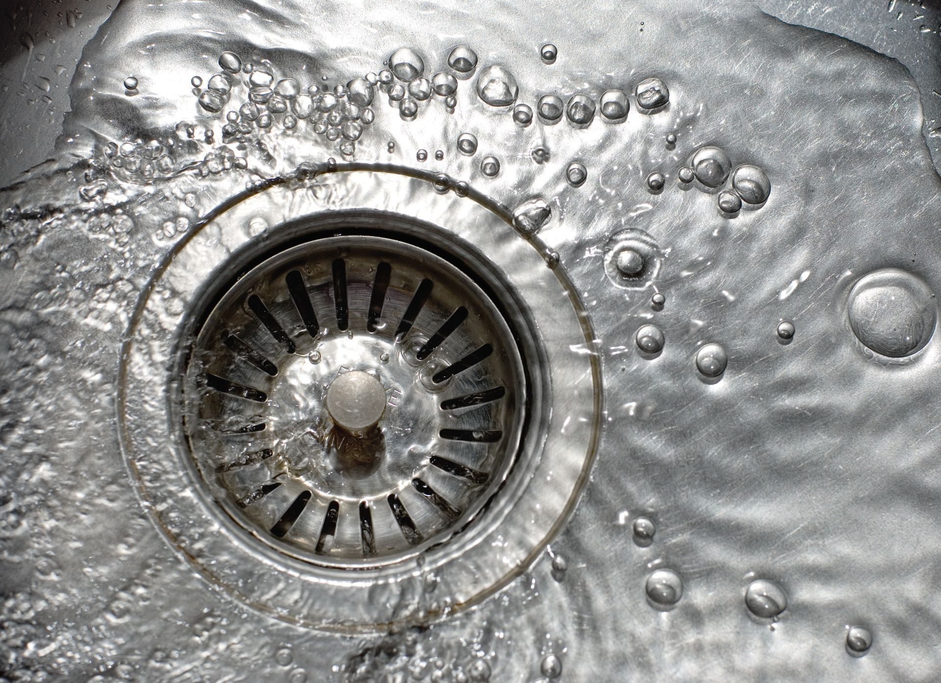 Water flowing into a stainless steel kitchen sink drain.