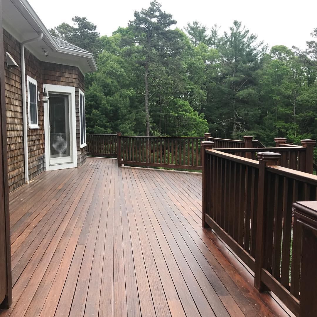 A large wooden deck with a railing and trees in the background