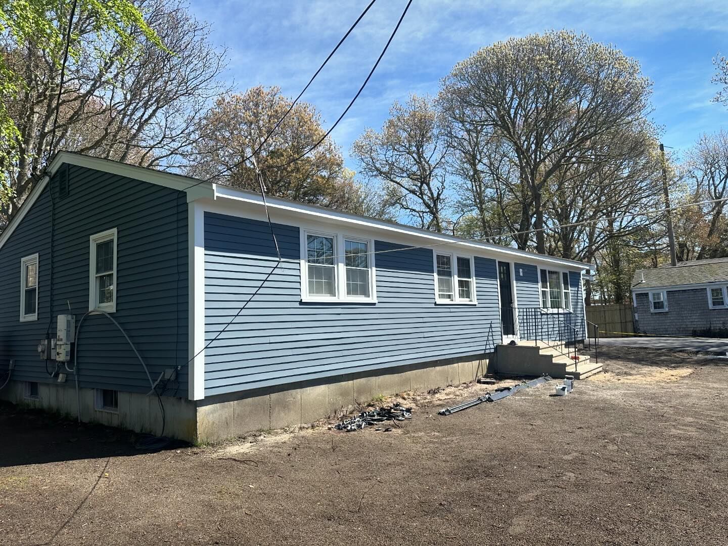 A blue house with white trim is sitting in the middle of a dirt field.