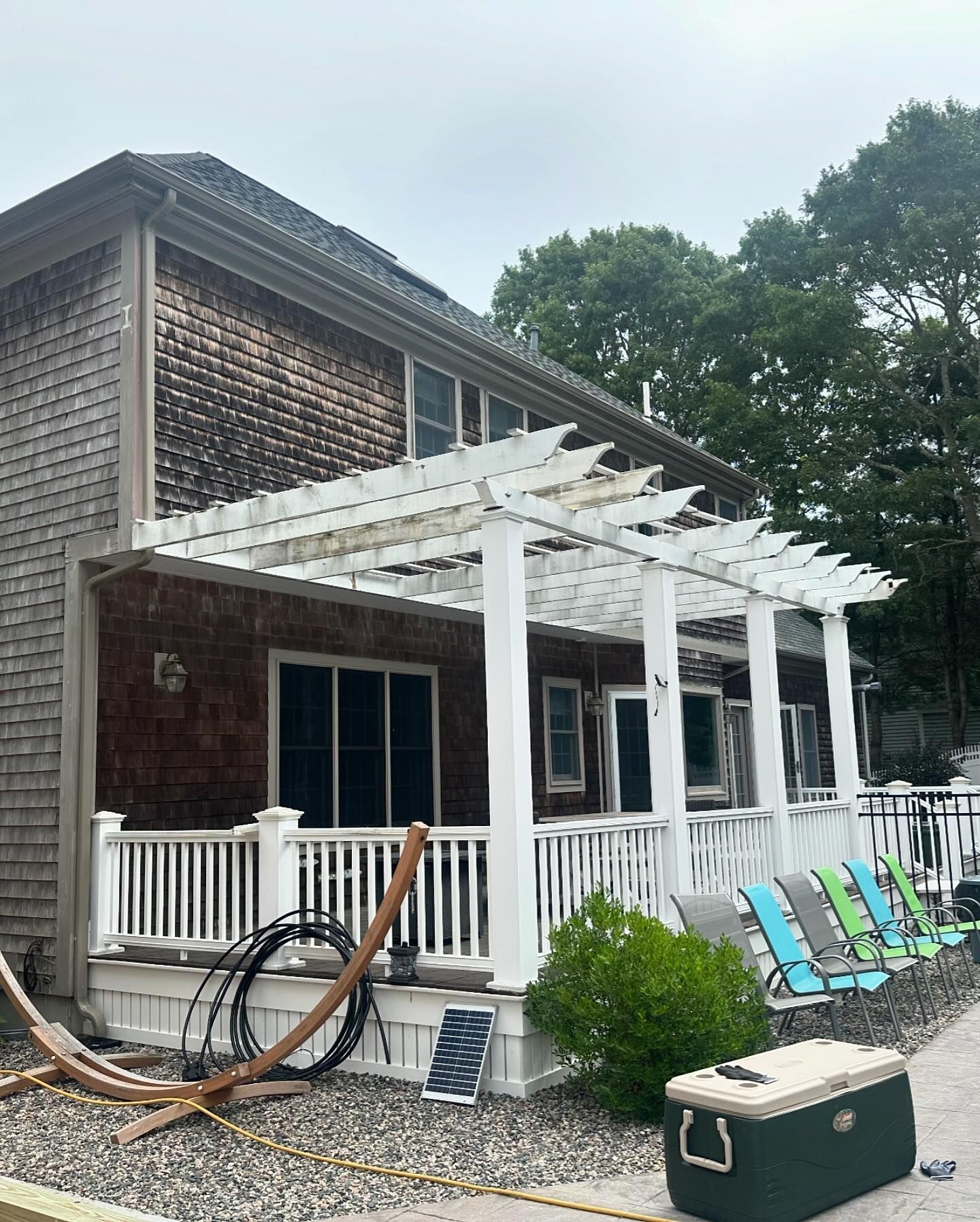 A house with a pergola and chairs on the porch.