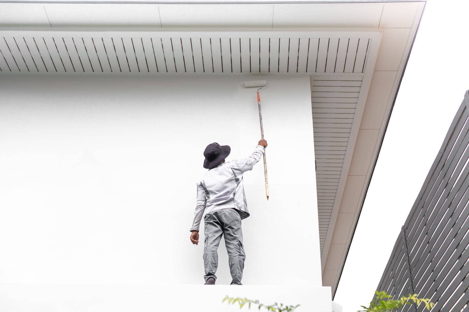 Painter using a roller on a wall under a building eave.