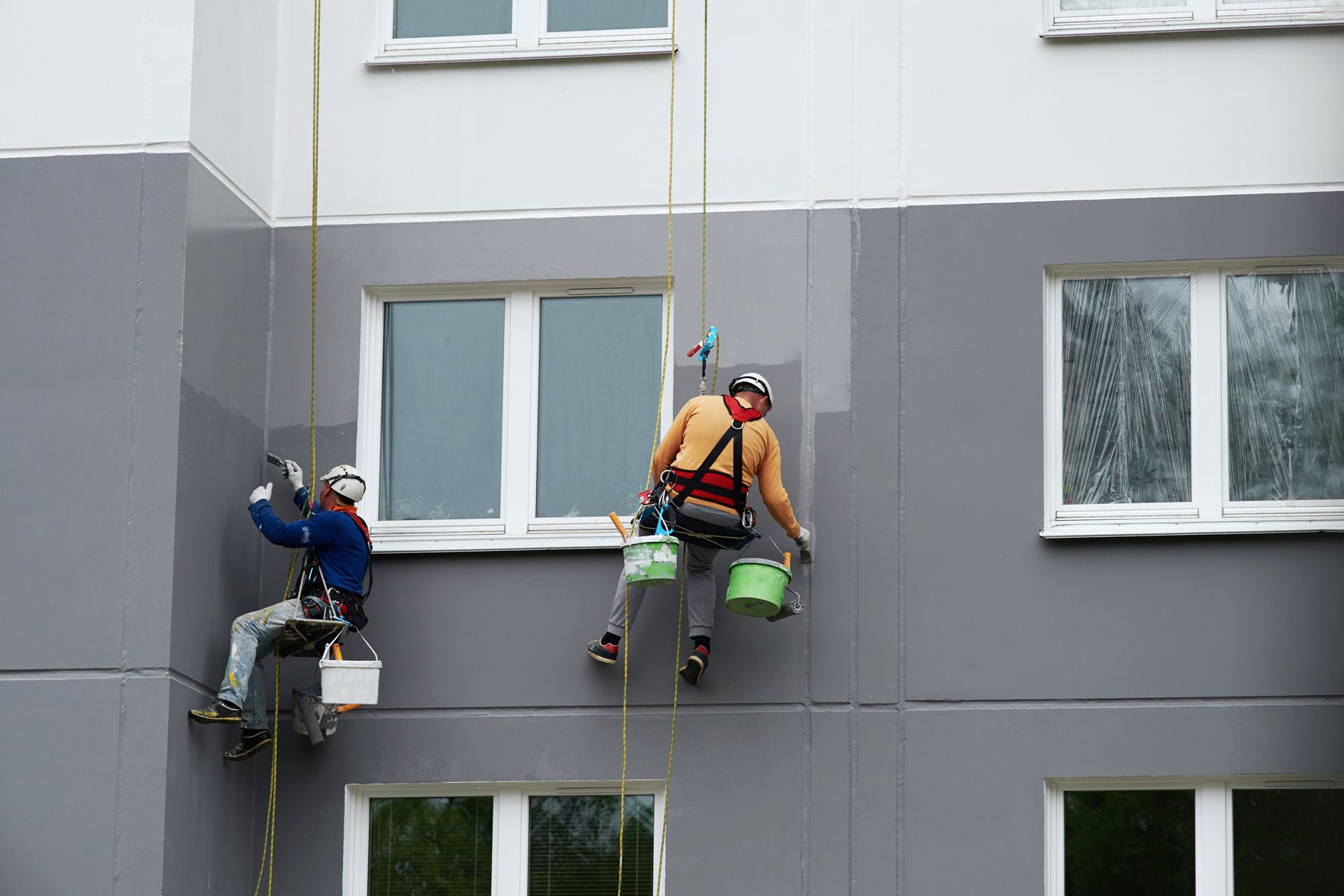 two men painting hanging while painting a wall of a building.