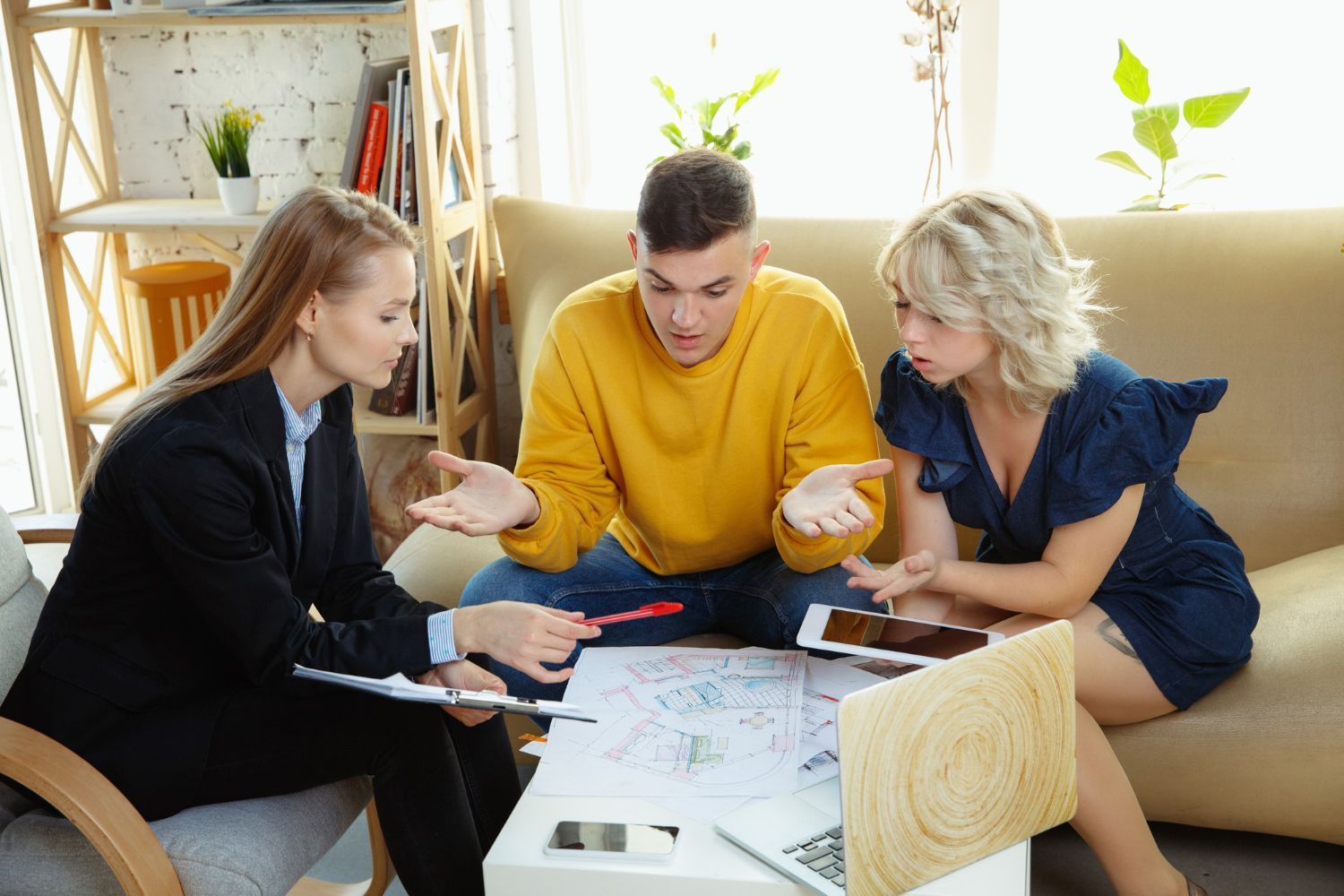 A woman in a suit consults with a couple over a table with papers, expressions of concern.