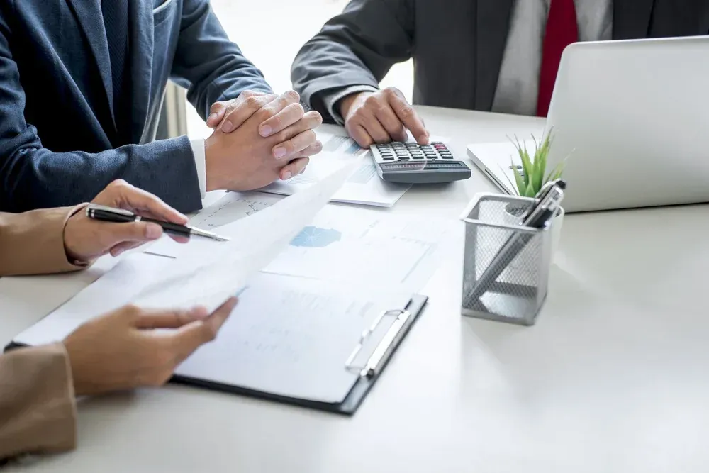 People in business attire reviewing documents, using a calculator, and working at a desk.