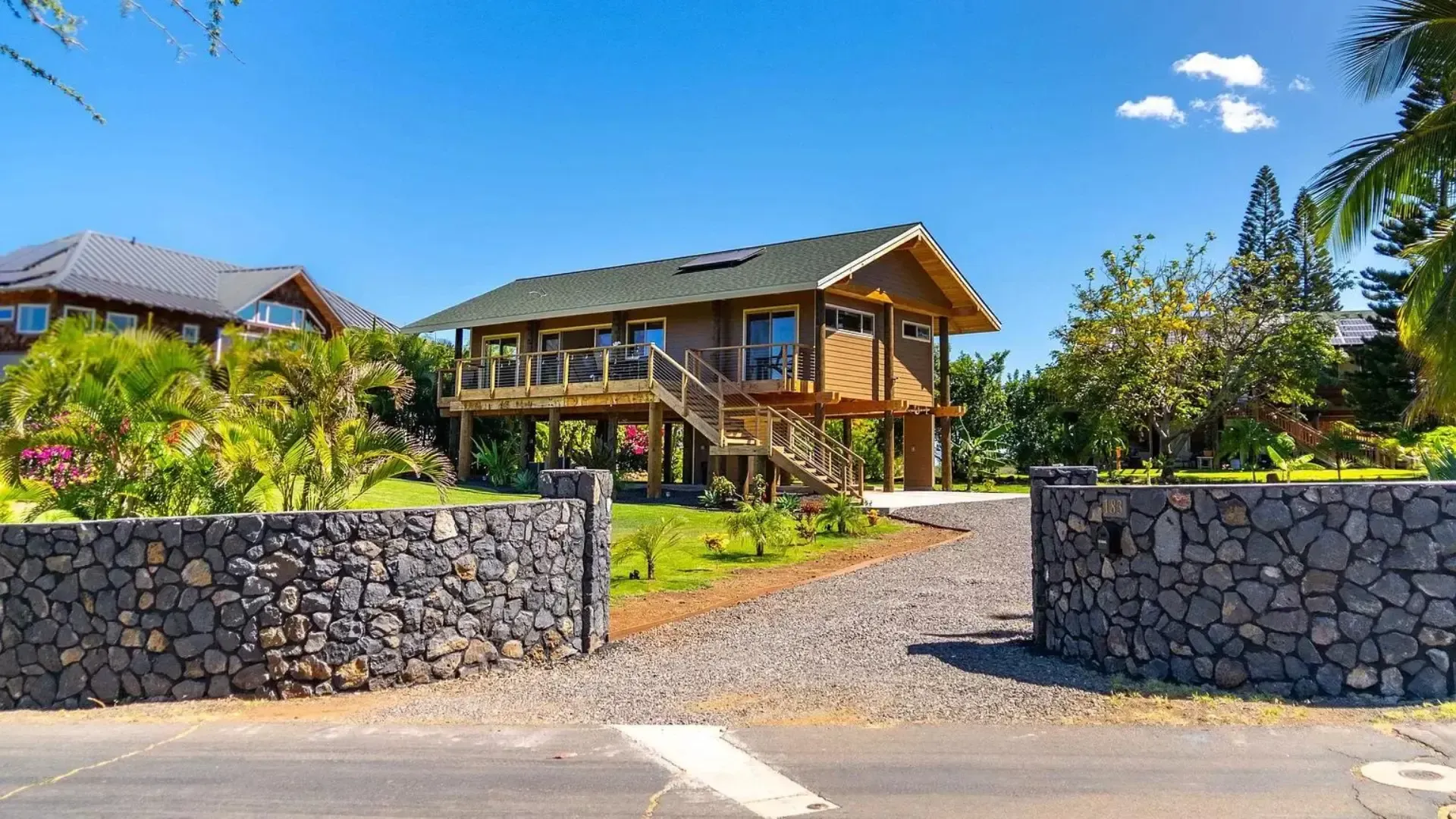 Wooden house with elevated deck and dark stone entrance, blue sky.