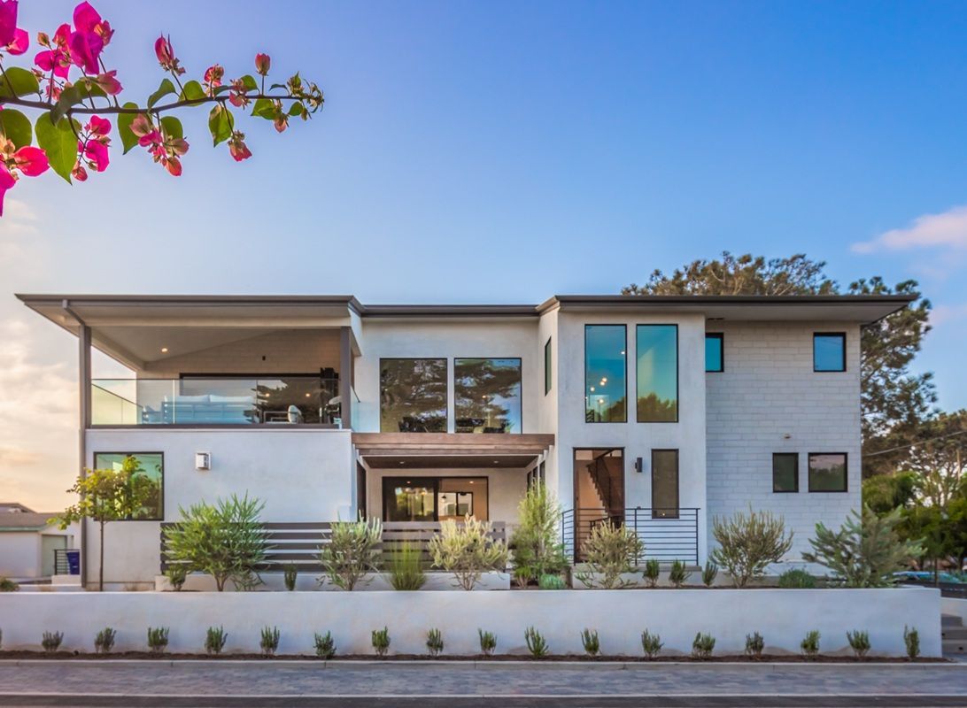 Modern two-story house with white exterior, balcony, and clear blue sky.