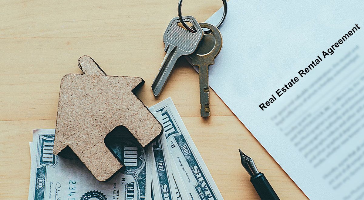 Rental agreement, keys, toy house, cash, and pen on a wooden surface.