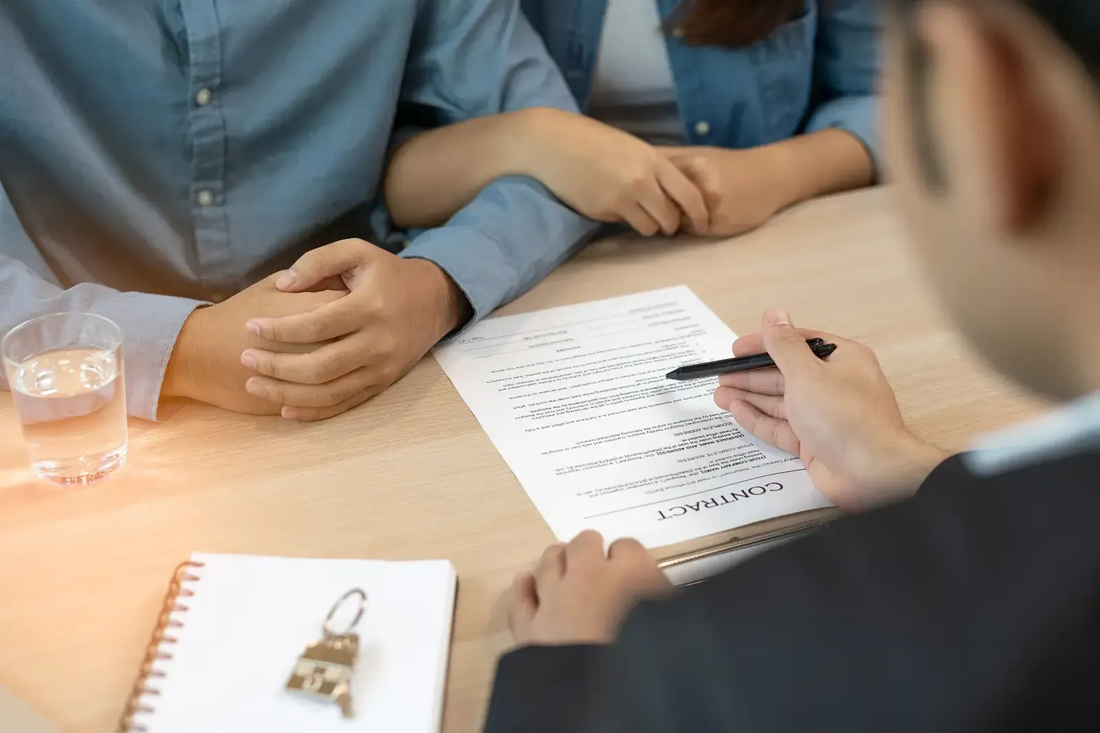 Couple holding hands while signing a document with a professional at a desk.