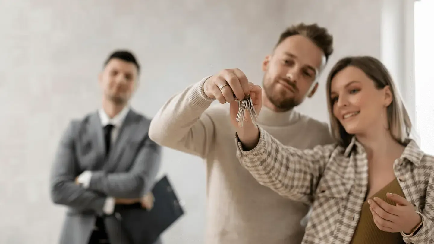 Couple holding keys with real estate agent in background.