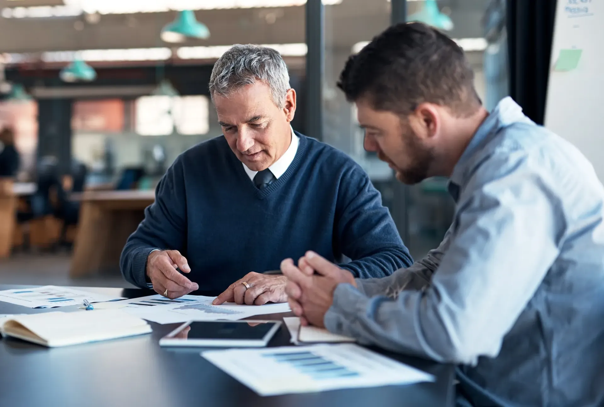 Two men reviewing documents at a table in an office setting.