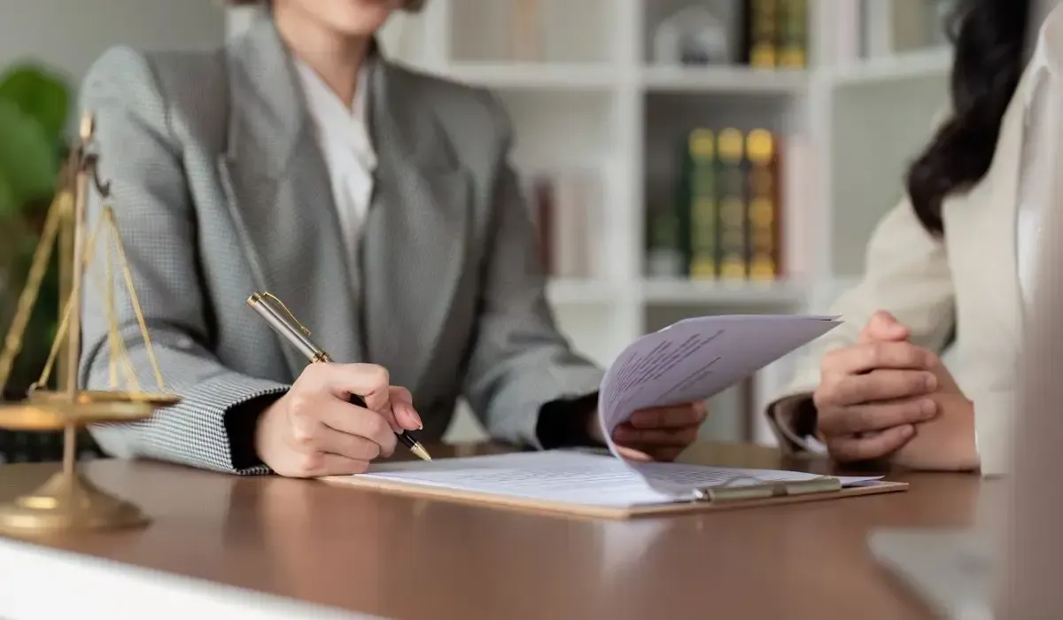 Two people in business suits reviewing documents at a desk, with a scale of justice.