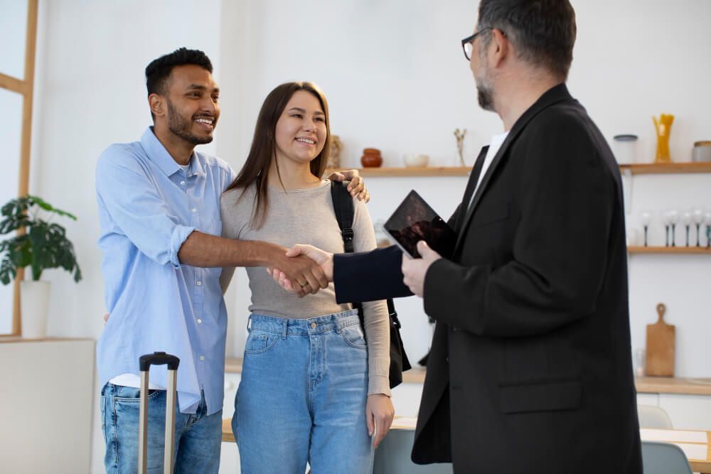 Couple shaking hands with a man holding a tablet indoors. They are smiling.