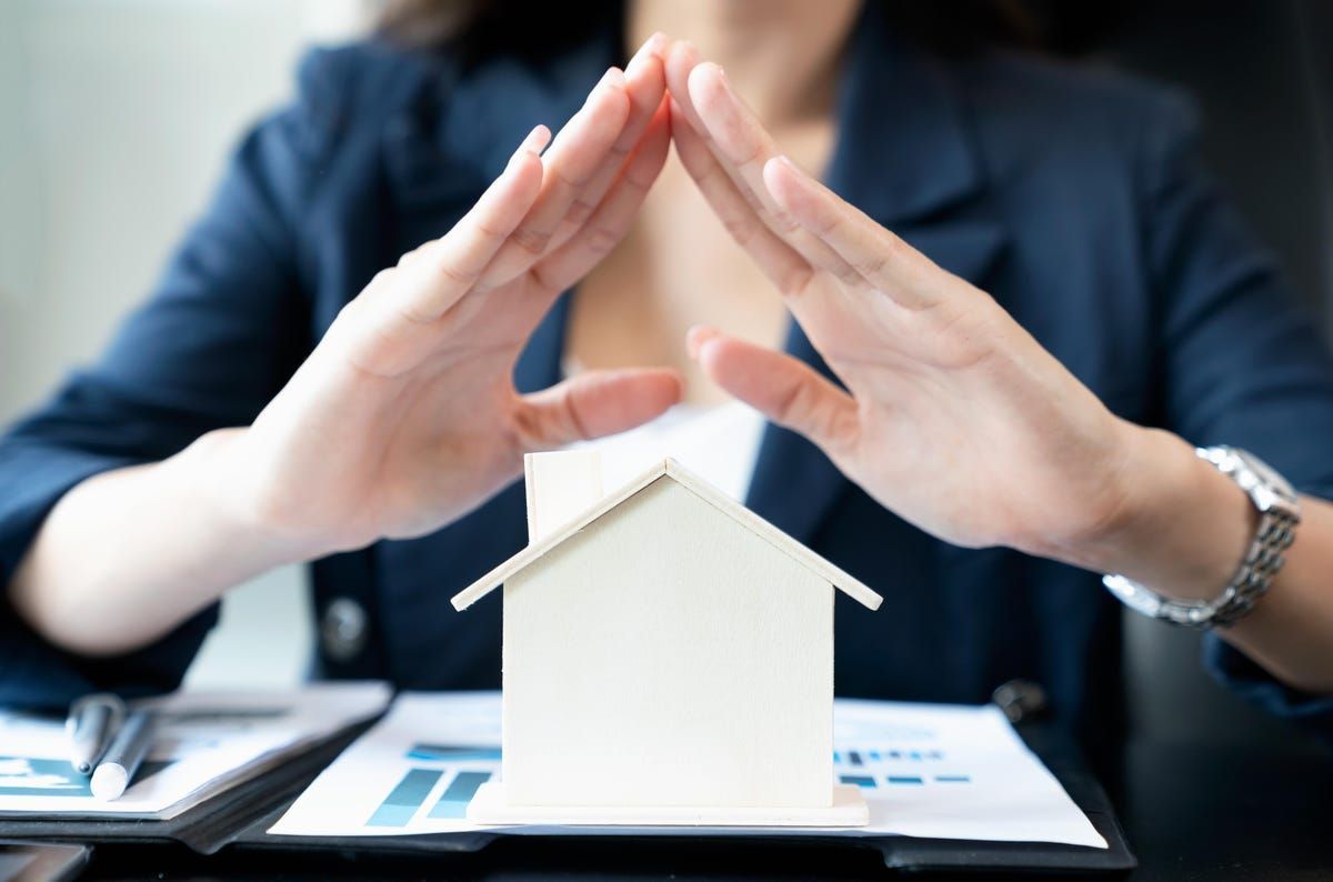 Woman's hands protect a small model house on a desk with papers.