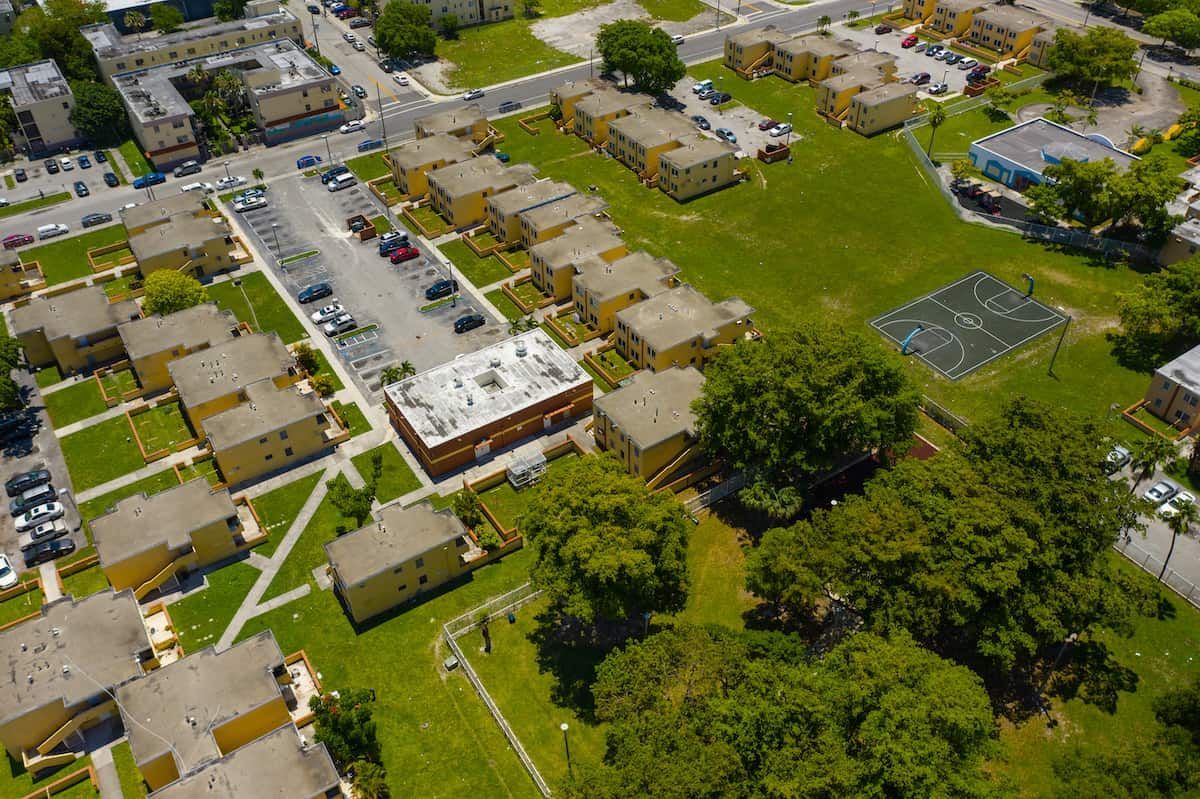 Aerial view of yellow apartment buildings with green space and a parking lot.