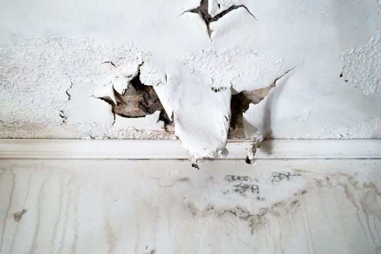 A white wall with peeling paint and a hole in it.