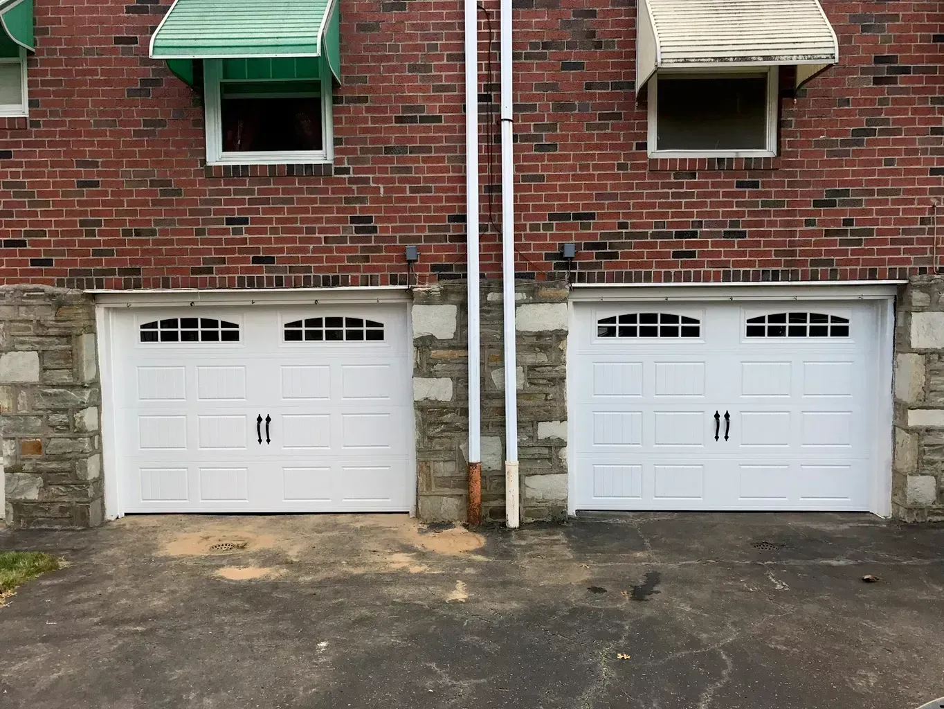 Two white garage doors are sitting next to each other in front of a brick building.