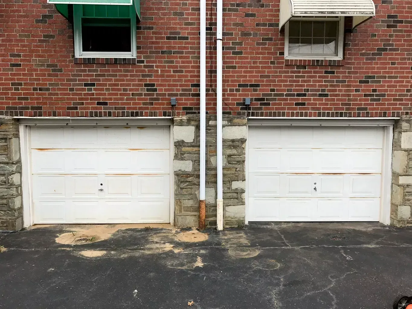 Two white garage doors are next to each other in front of a brick building.