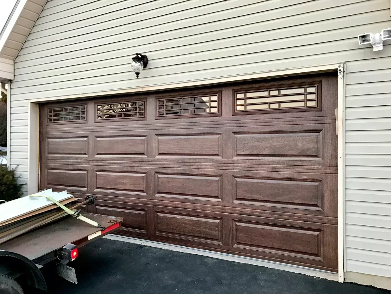 A brown garage door is open and a trailer is parked in front of it.