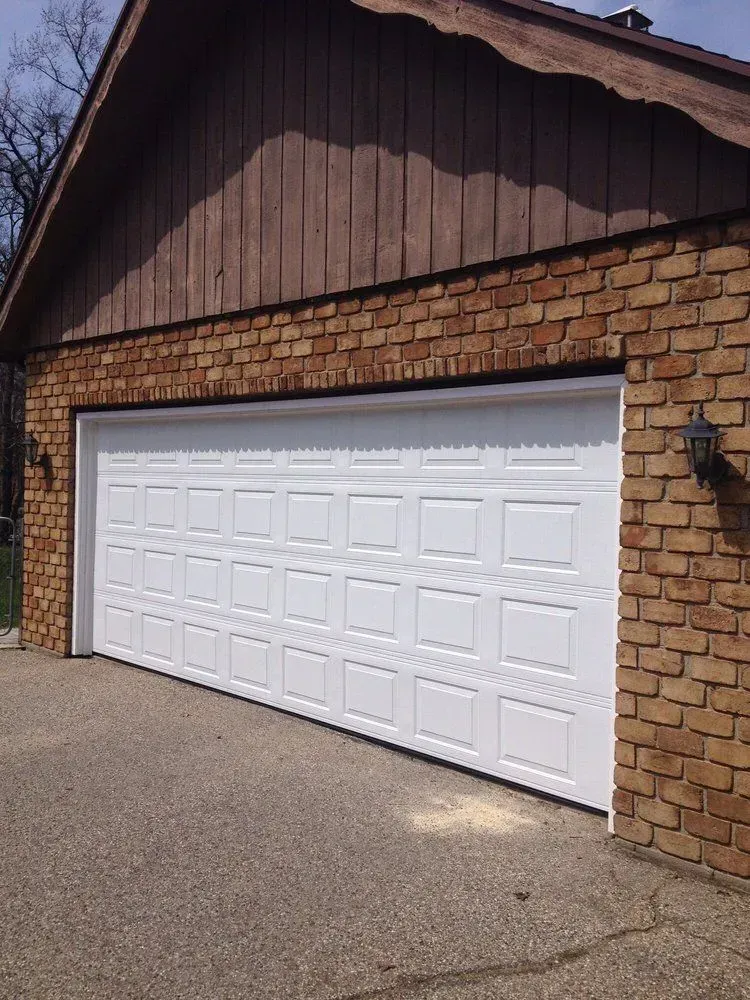 A white garage door is sitting in front of a brick building.