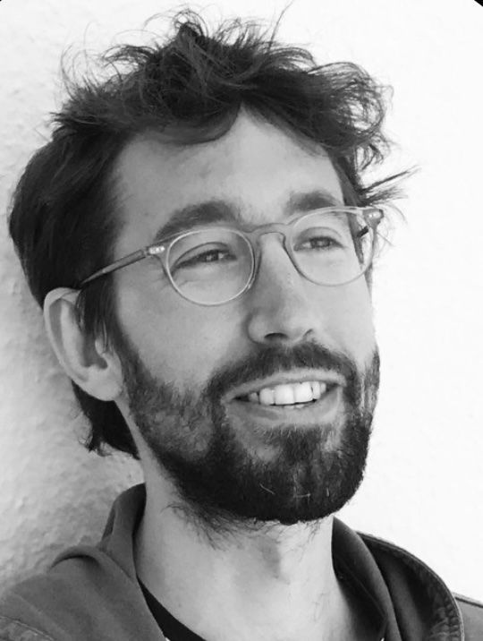 Felix de Rosen with glasses and beard smiles, looking off-camera.