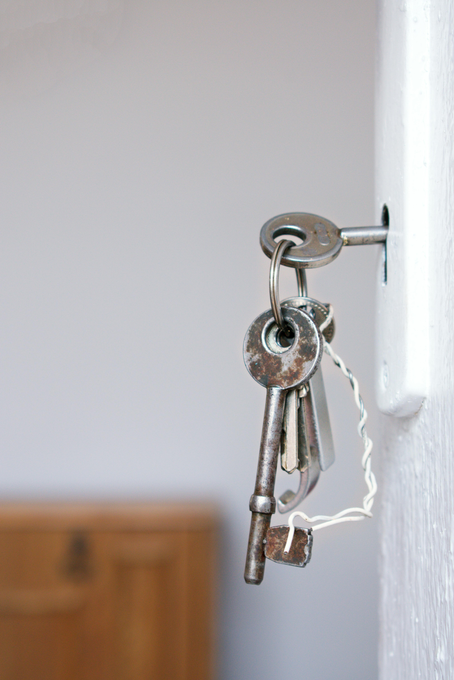 Keys in a door lock, one inserted, other keys hanging below. White door, neutral background.