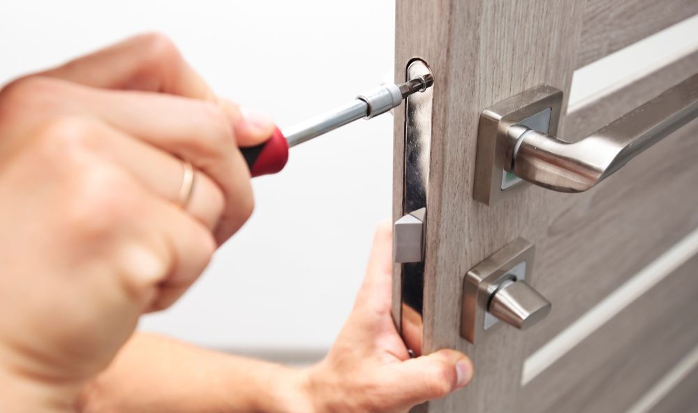 Person uses screwdriver to install a silver door handle on a light wooden door.