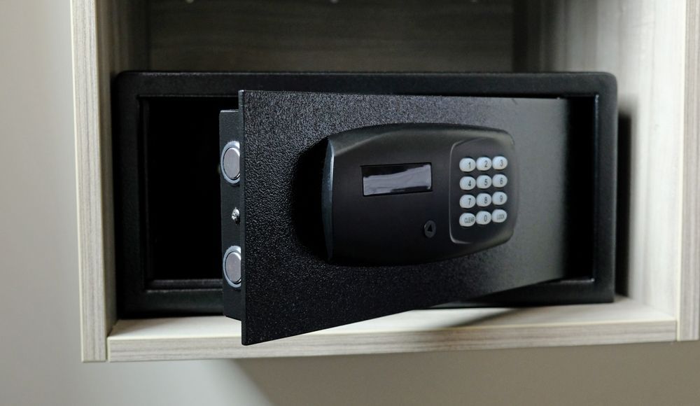 Black safe with open door and keypad inside a light-colored cabinet.