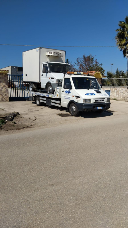 Carro attrezzi che trasporta un camion con cassone bianco in una giornata di sole.