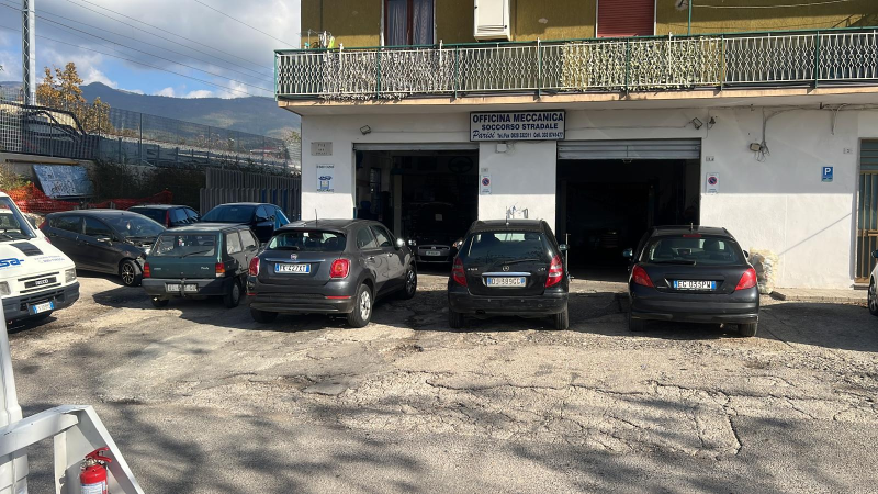 Auto parcheggiate fuori da un garage, montagne sullo sfondo. Il garage ha una porta aperta.