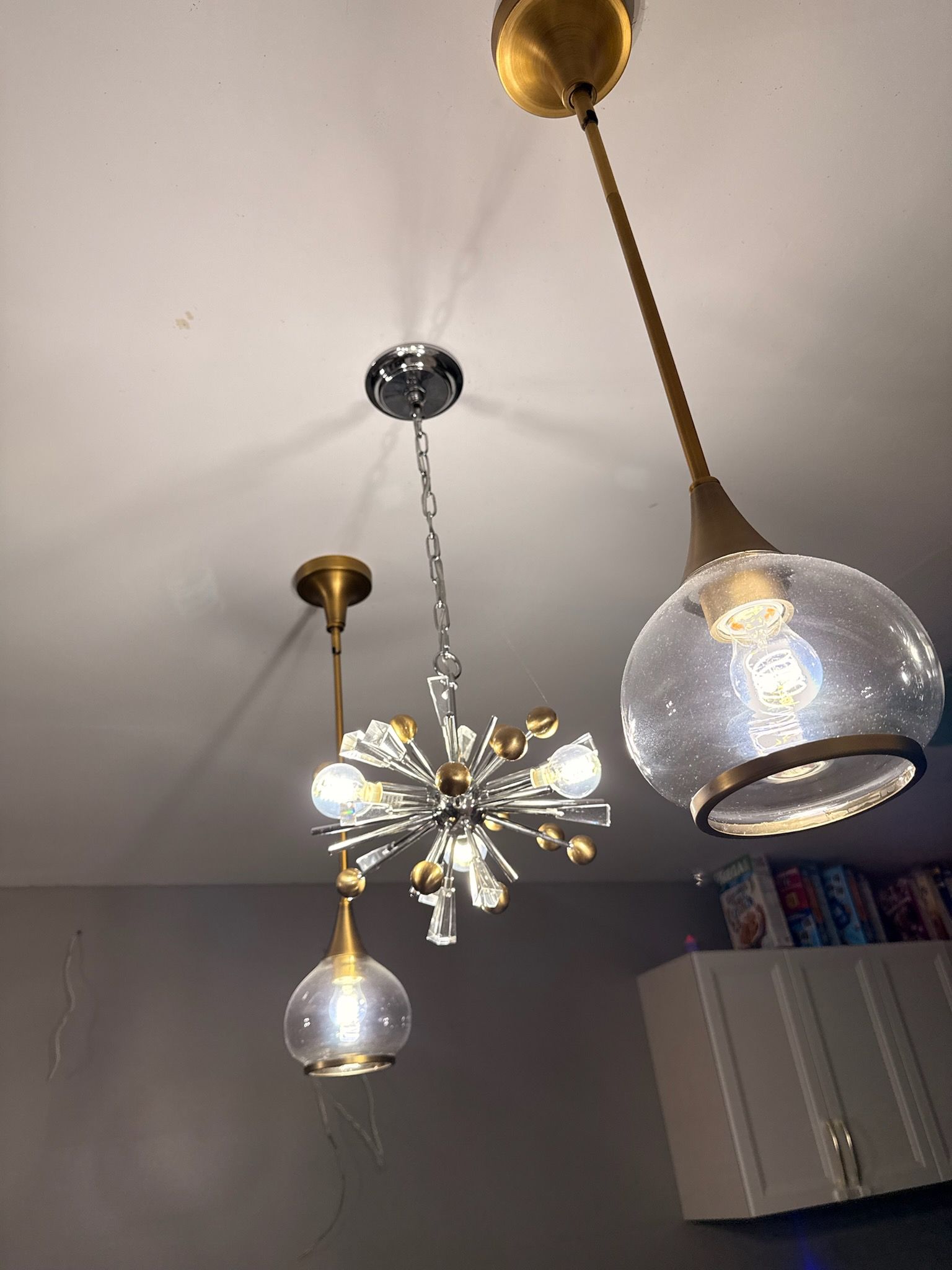 Modern ceiling light fixtures, including a starburst chandelier and pendant lamps, in a room with gray cabinets