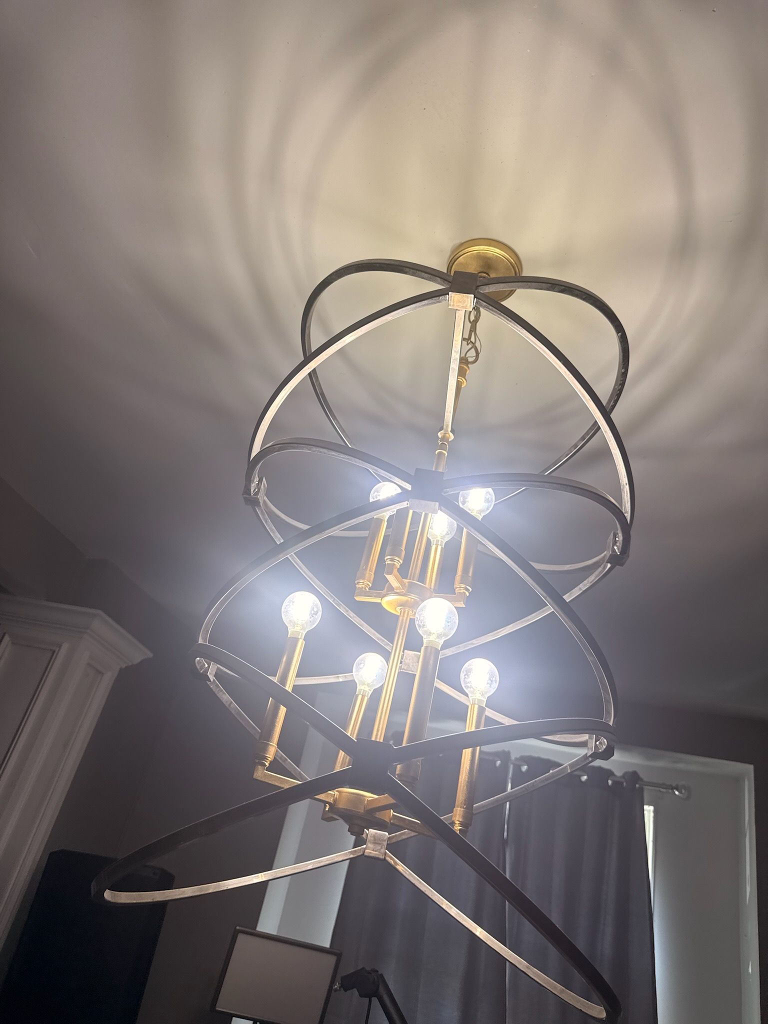 Modern chandelier with glowing bulbs and circular metal rings, viewed from below against a ceiling.