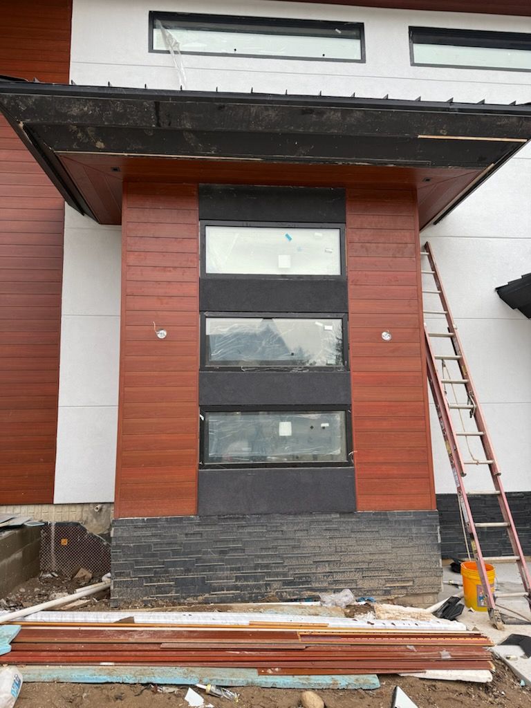 Front view of a modern house entry with wood siding, black trim, and a ladder leaning on the right side.