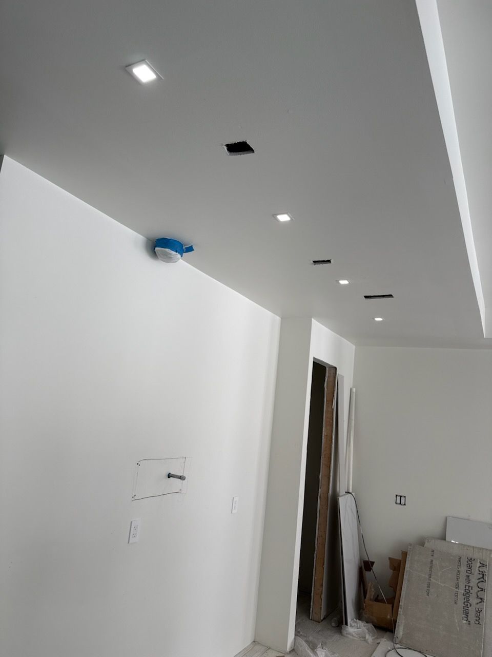 Interior hallway with white walls and recessed ceiling lights, partially renovated and cluttered with materials.