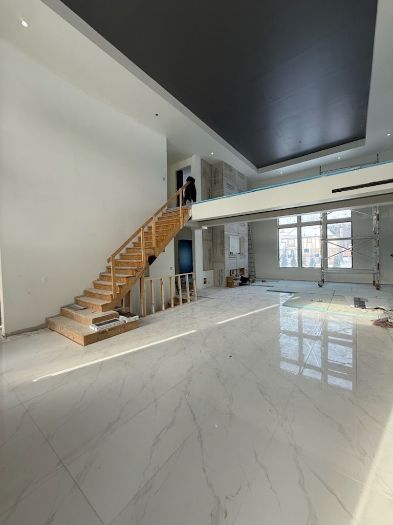 Bright modern open-plan room with glossy white floor, staircase, and large windows.
