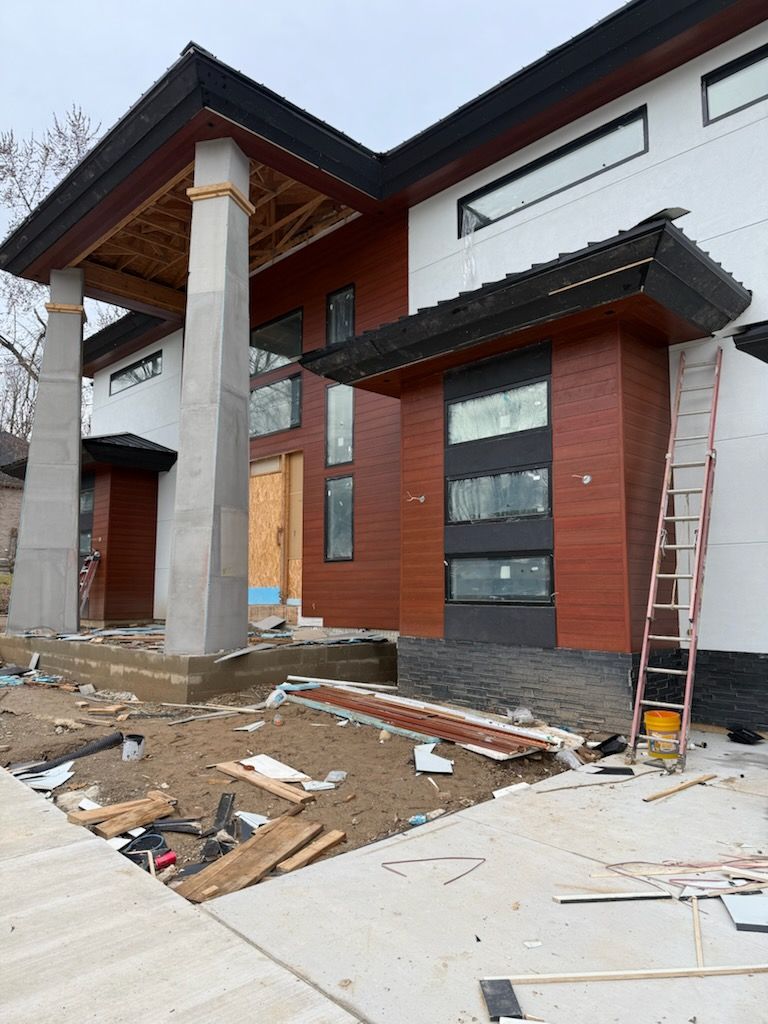 Modern house exterior under construction, with white and brick walls, wooden columns, and debris on the ground