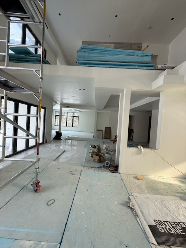 Interior of a modern house under renovation, with scaffolding, drywall, and construction materials throughout the room.
