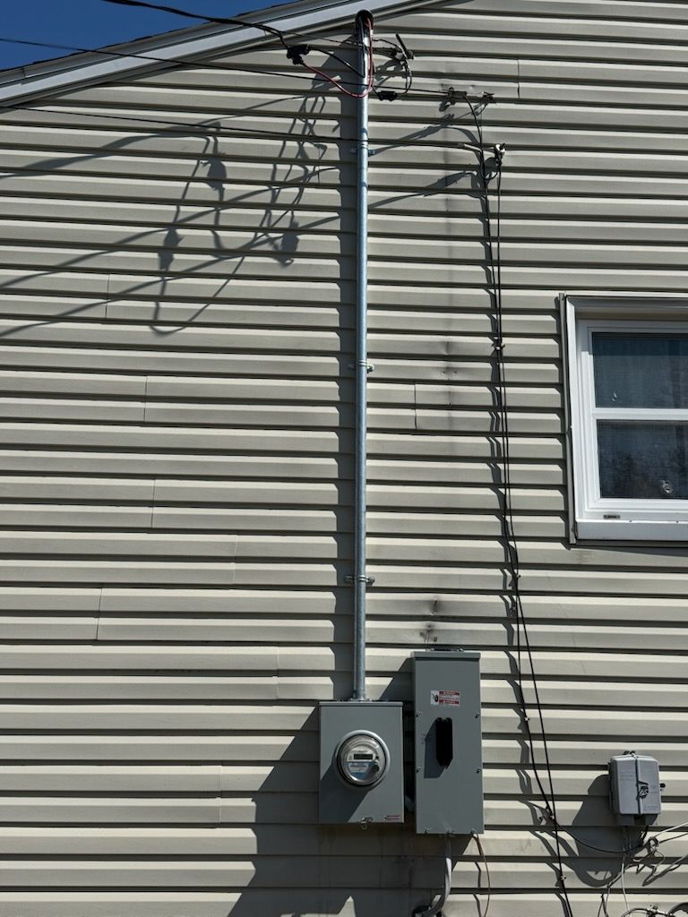 Utility meter and electrical boxes on a beige house wall beneath overhead cables.