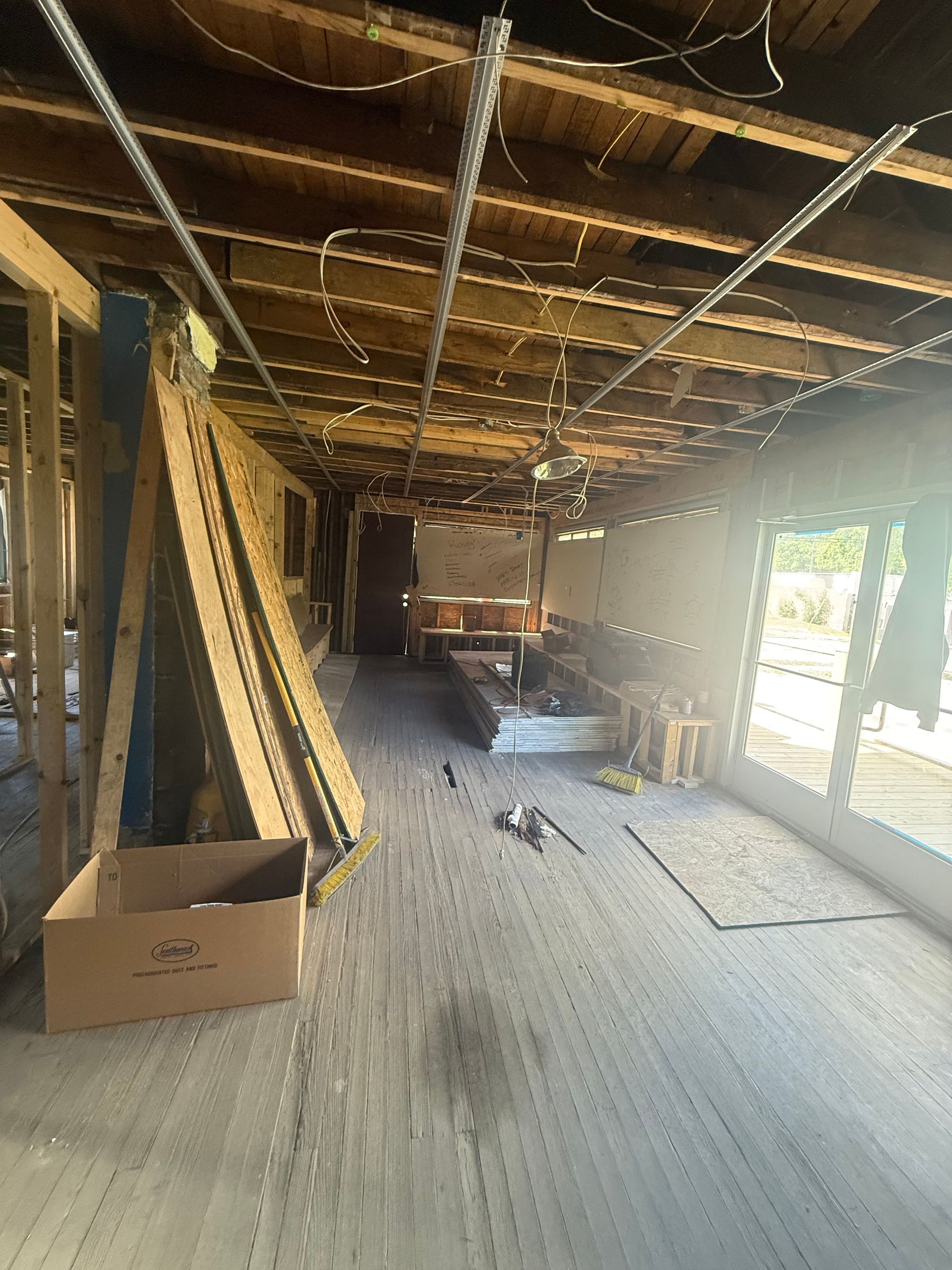 Unfinished room with exposed ceiling beams, scattered materials, and bright light from a doorway on the right.