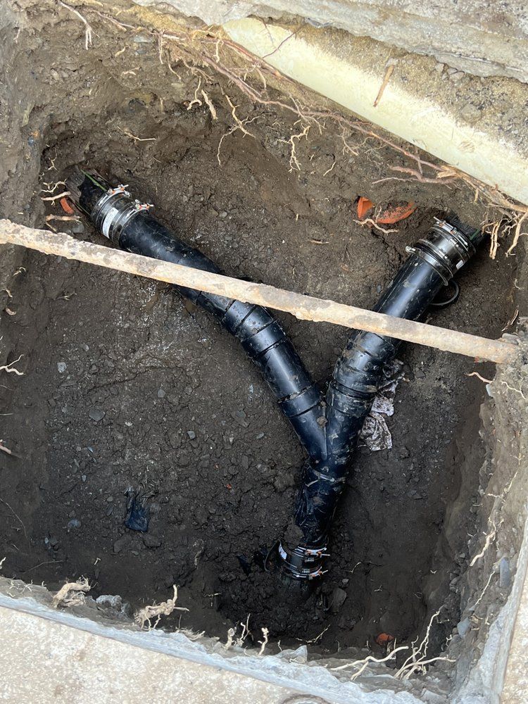 Two black pipes are laying in the dirt in a hole.