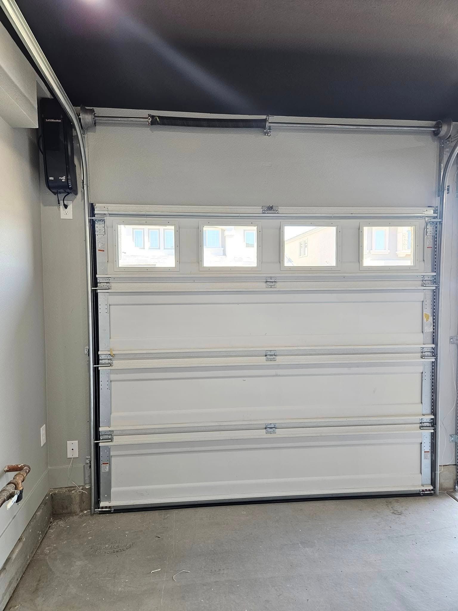 A white garage door with three windows is open in a garage.