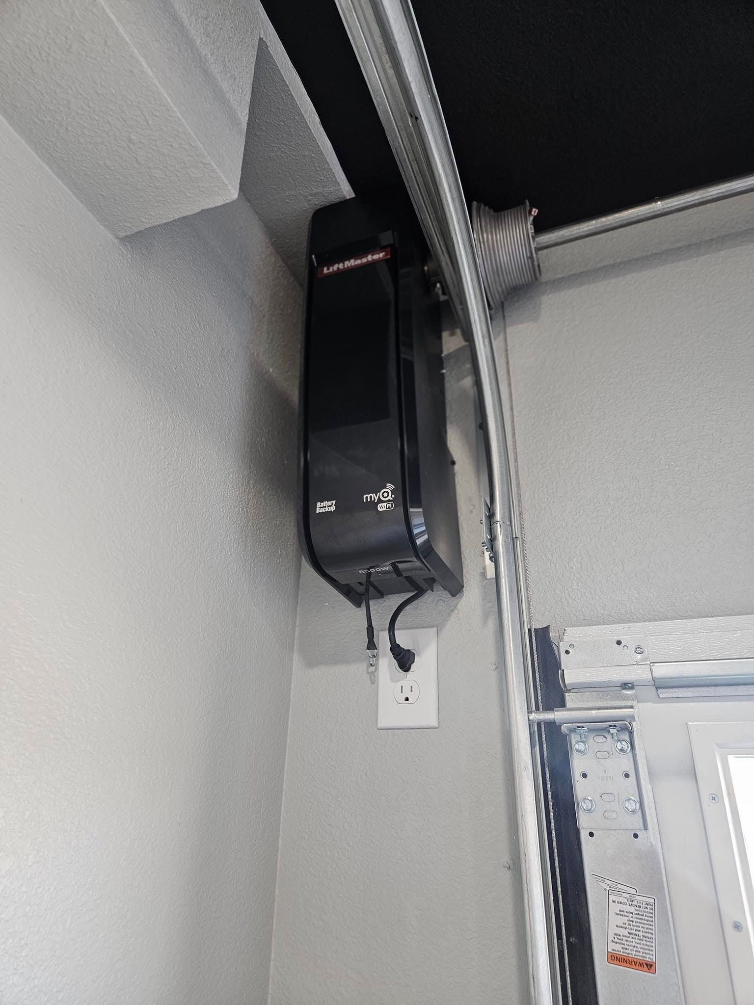 A black box is hanging from the ceiling of a garage door.