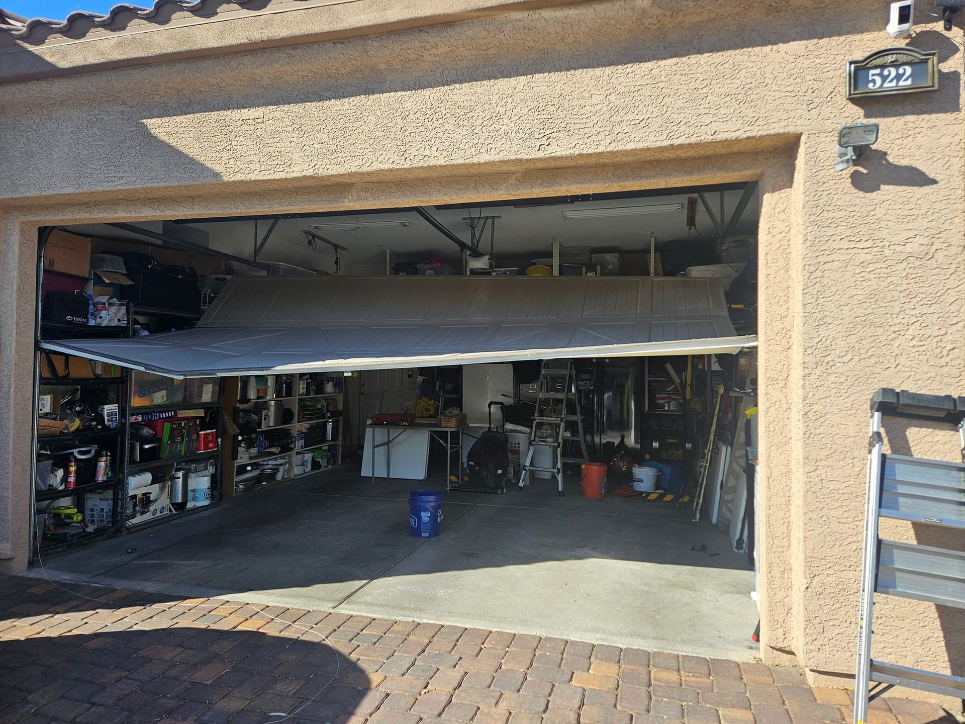 A garage with a garage door open and a ladder in front of it.