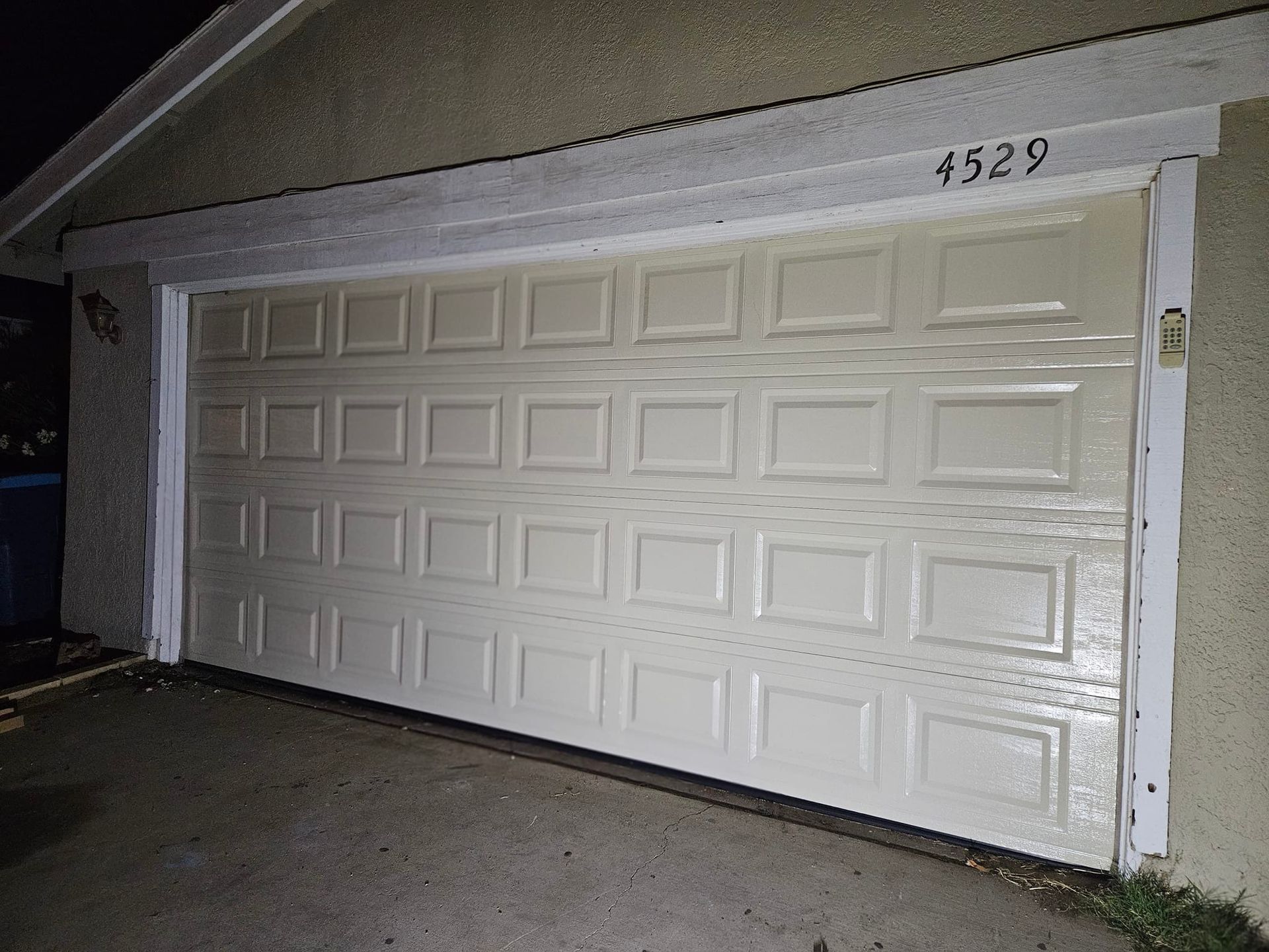 A white garage door is open to a house at night.