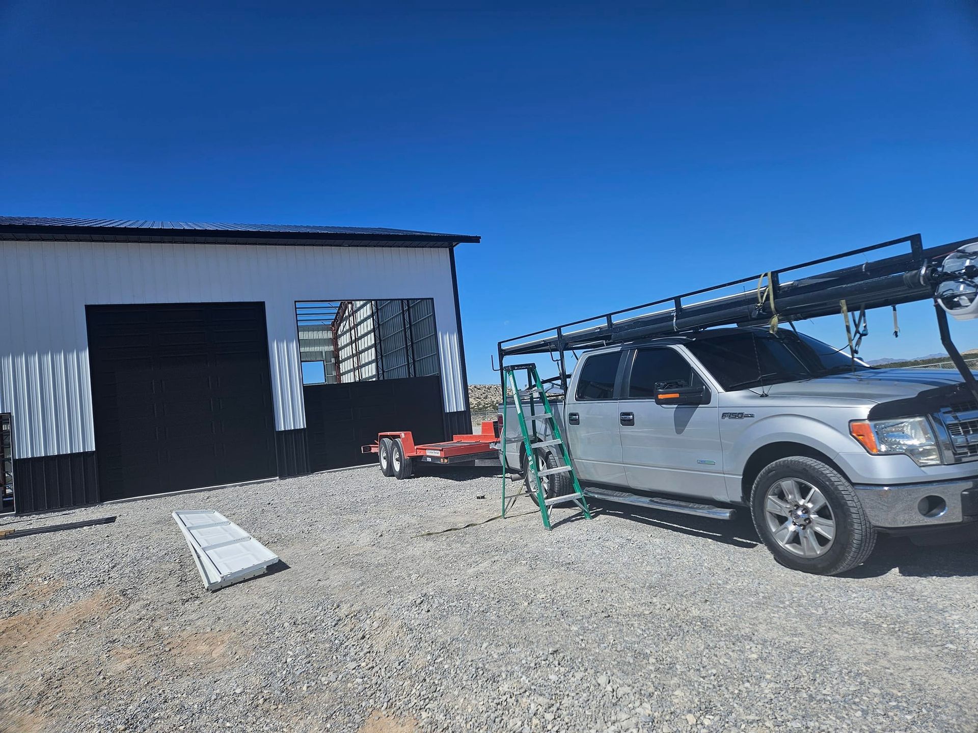 A silver truck with a ladder on the roof is parked in front of a building.